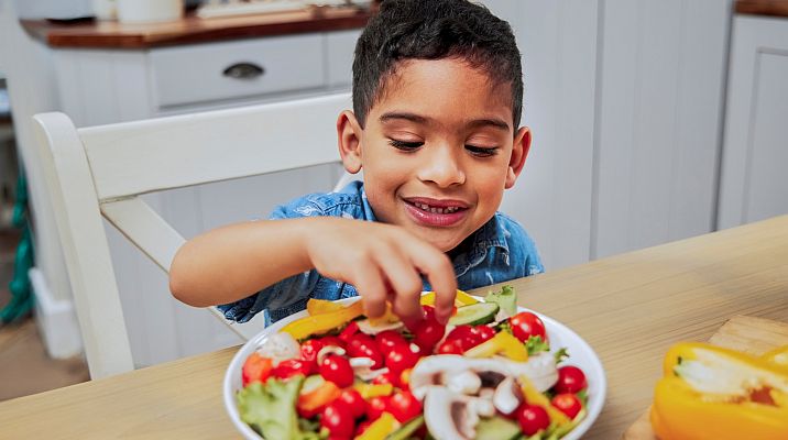 boy picking from a plate of colorful vegetables